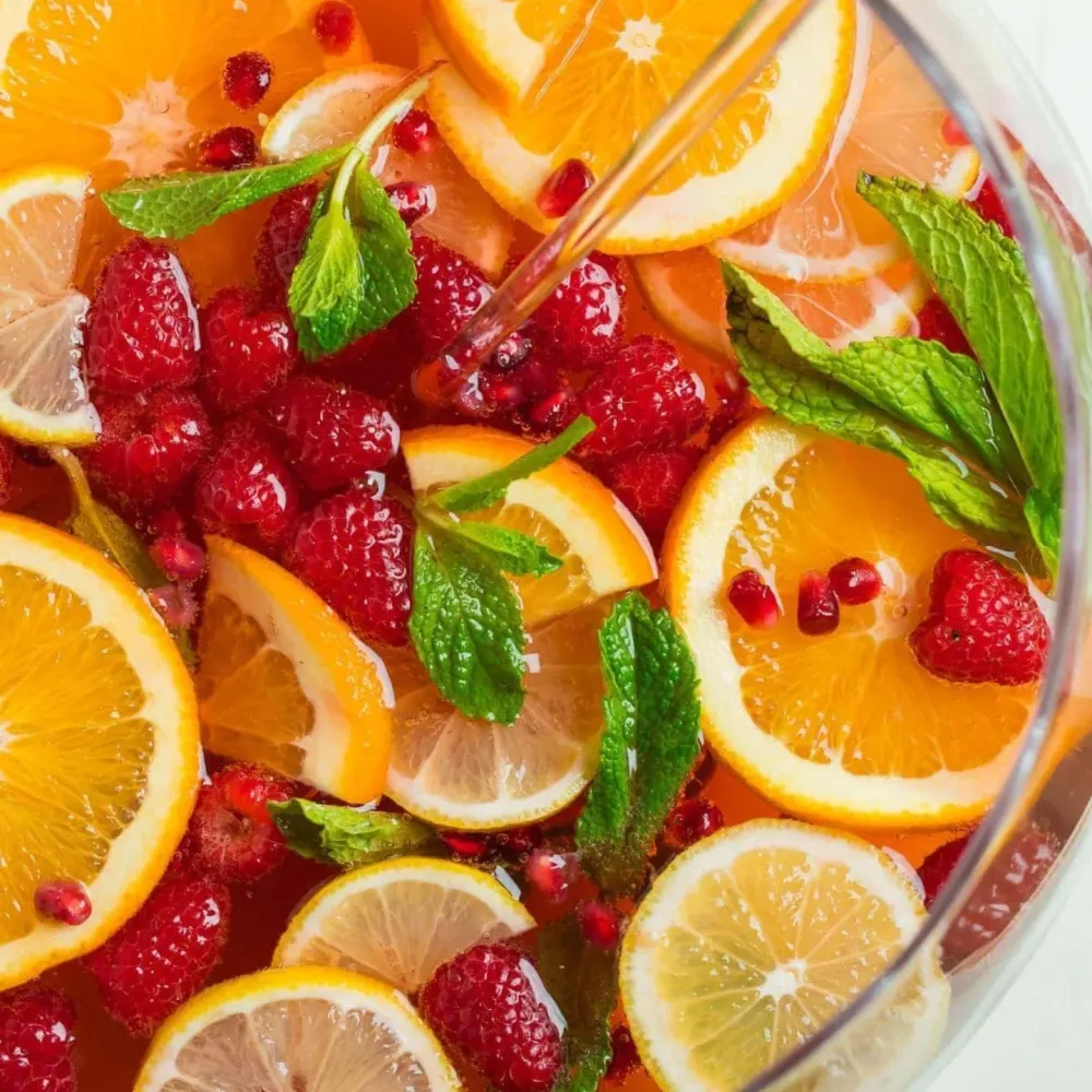 A bowl of fresh punch with raspberries, citrus slices, and mint